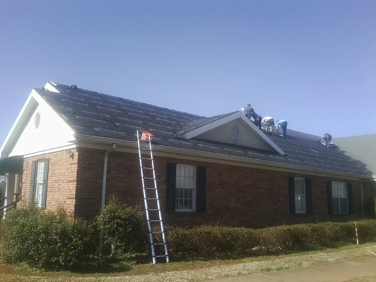 Crew tearing shingles off a brick ranch roof with a ladder set — Emergency Roof Repair work by our crew in Montrose