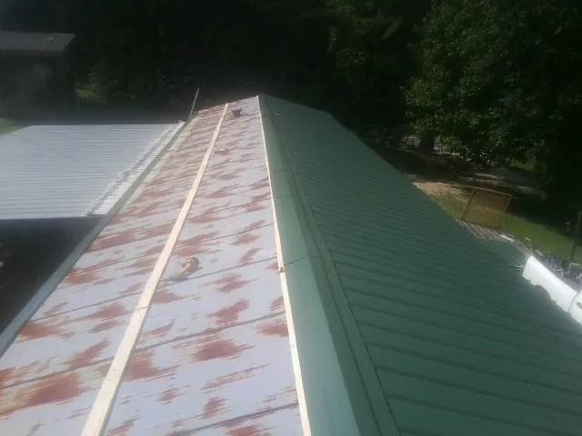 Old rusted panels beside newly installed green metal roofing — Wind Damage Roof Repair by Roofing Brothers in Montrose