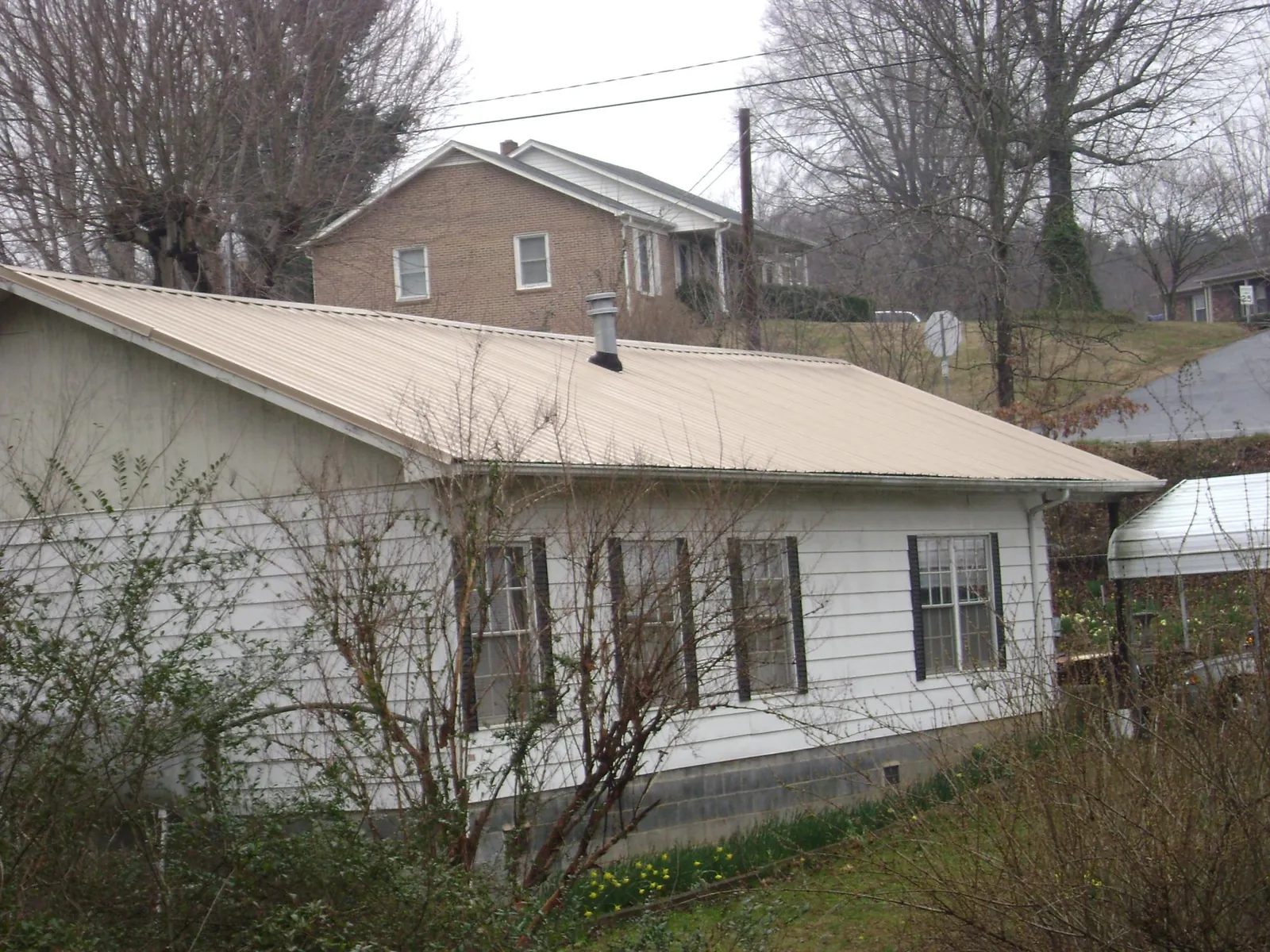 Tan metal roof on a white sided house set into a hillside — Commercial Roofing by Roofing Brothers in Montrose